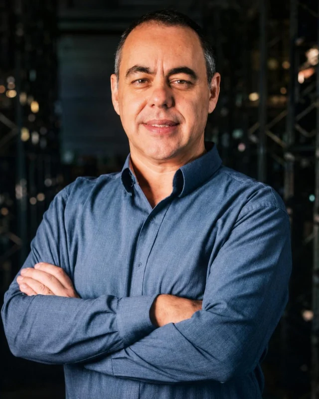 Miguel Rossato, de camisa azul e braços cruzados, num galpão industrial